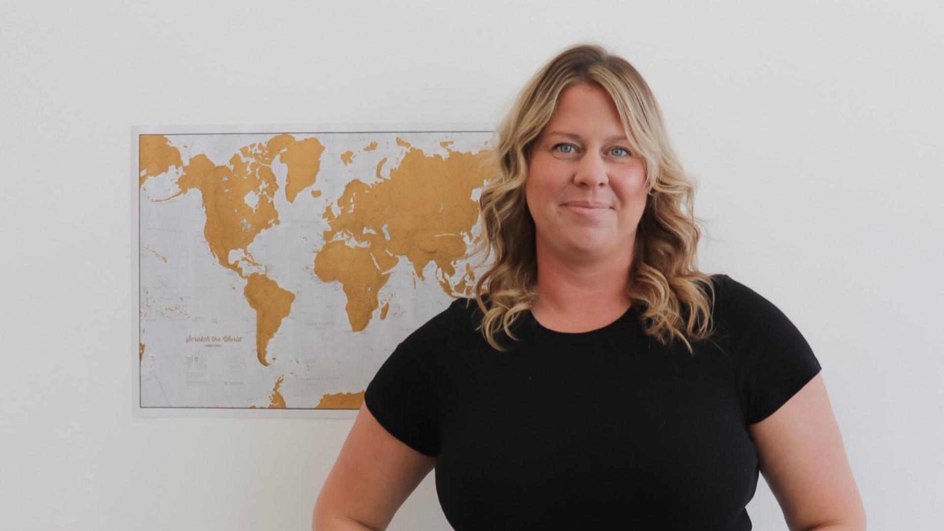 Madison stands in front of a map on the wall in a black t-shirt.