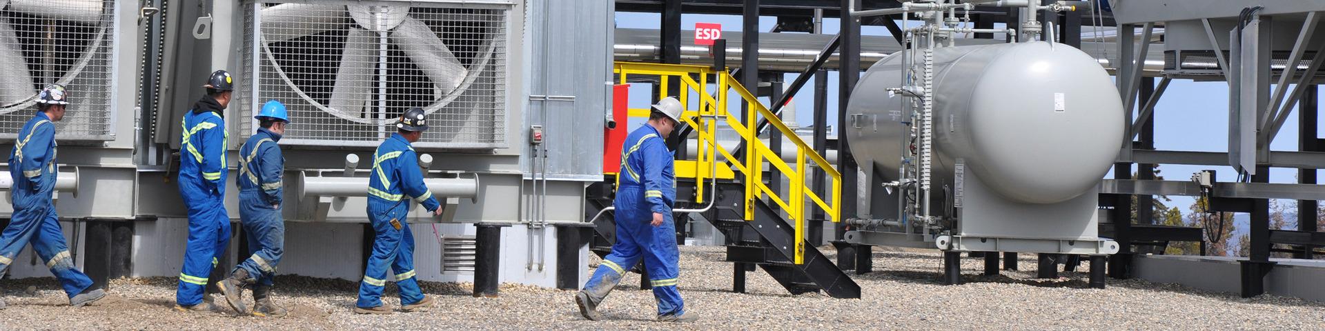 Workers in protective equipment walk across an industrial site.